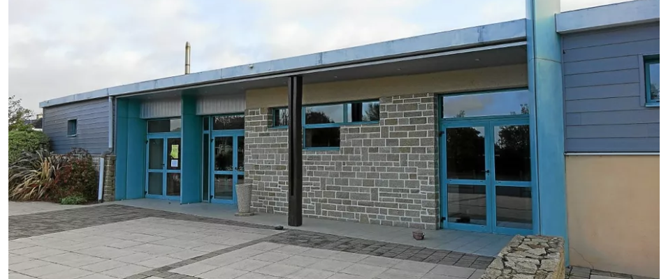Bâtiment avec murs en brique, portes bleues, et toiture plate. Pavage devant l'entrée.
