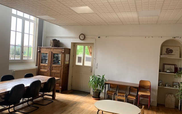 Salle avec tables, chaises, armoire, étagères, plantes et porte.