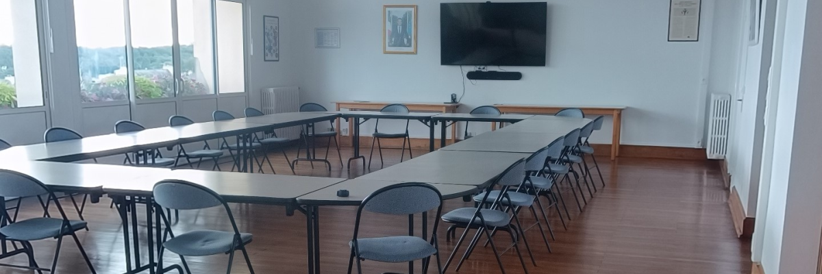 Salle avec tables, chaises, écran, haut-parleurs et fenêtres.