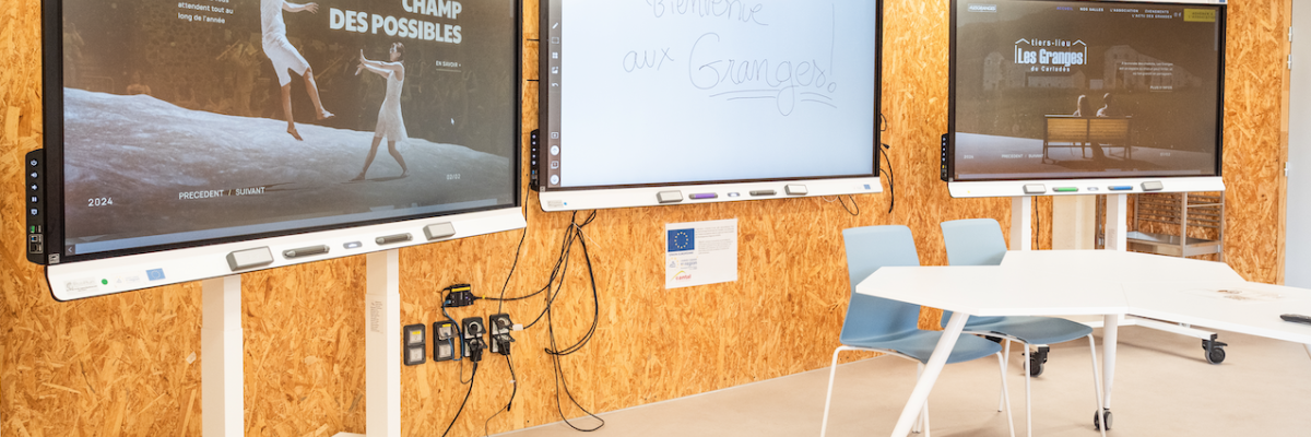 Salle avec trois tableaux interactifs, une table, des chaises et un mur en bois.