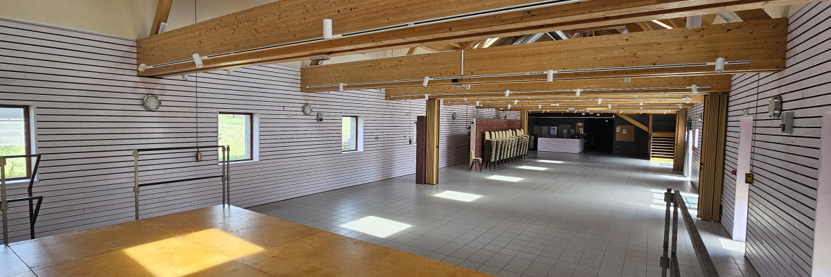 Salle spacieuse avec poutres apparentes, sol en bois, murs en brique, rampes et fenêtres.
