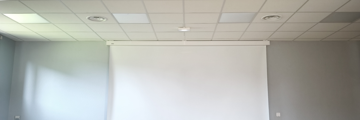 Salle avec projecteur, écran, parquet et murs blancs.