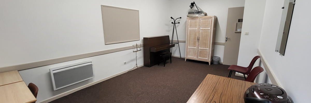 Salle avec tableau, piano, armoire, aspirateur, chaises et radiateur.