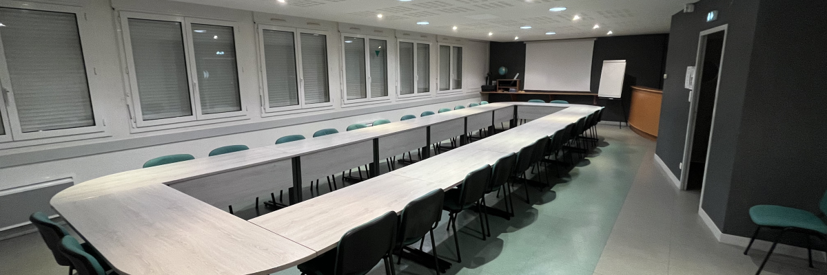 Salle de réunion avec table en U, chaises, écran, vidéo projecteur et ordinateur.