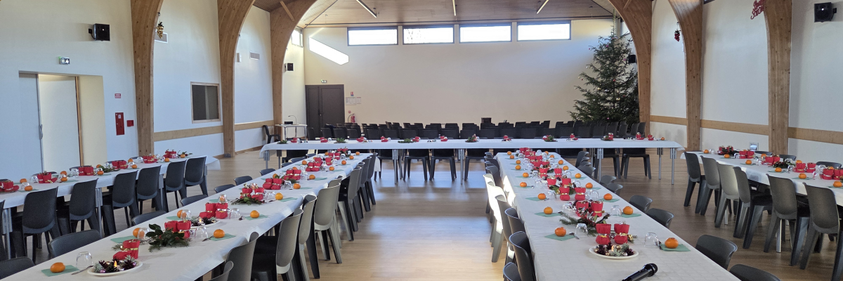 Salle avec tables, chaises, décoration de table, et arbre de Noël.