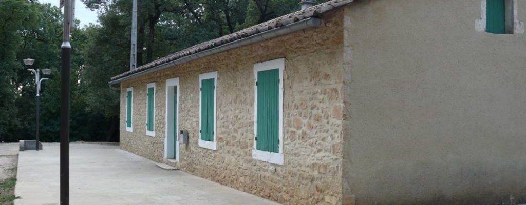 Bâtiment en pierre avec fenêtres vertes, allée et lampadaires.