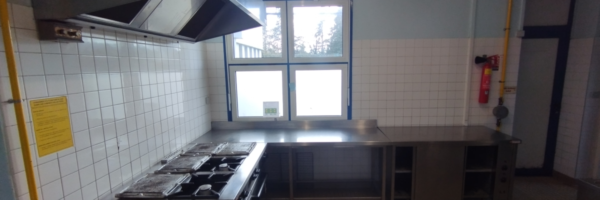 Cuisine industrielle avec hottes, plans de travail, étagères, fenêtres et extincteur.