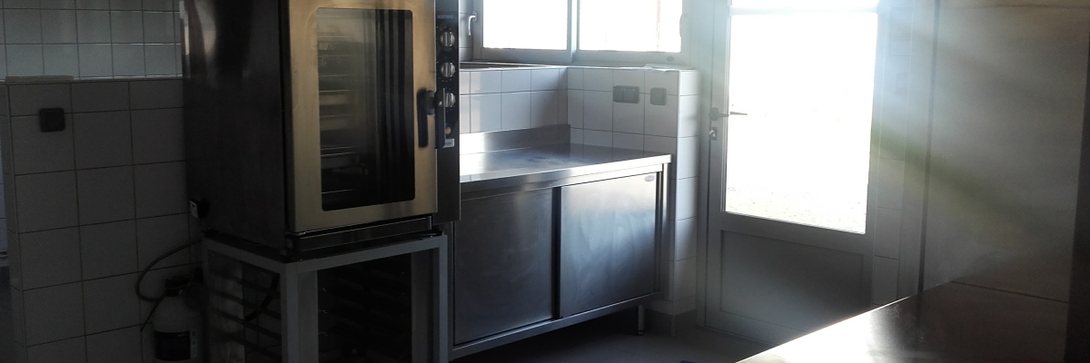 Cuisine équipée : four industriel, plans de travail, évier, porte.