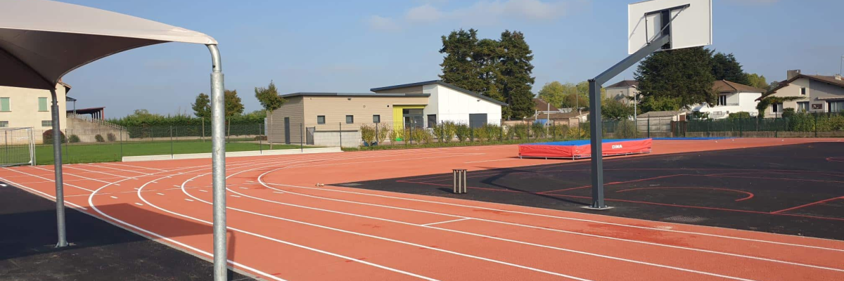 Stade avec piste d'athlétisme, panier de basket et abris.