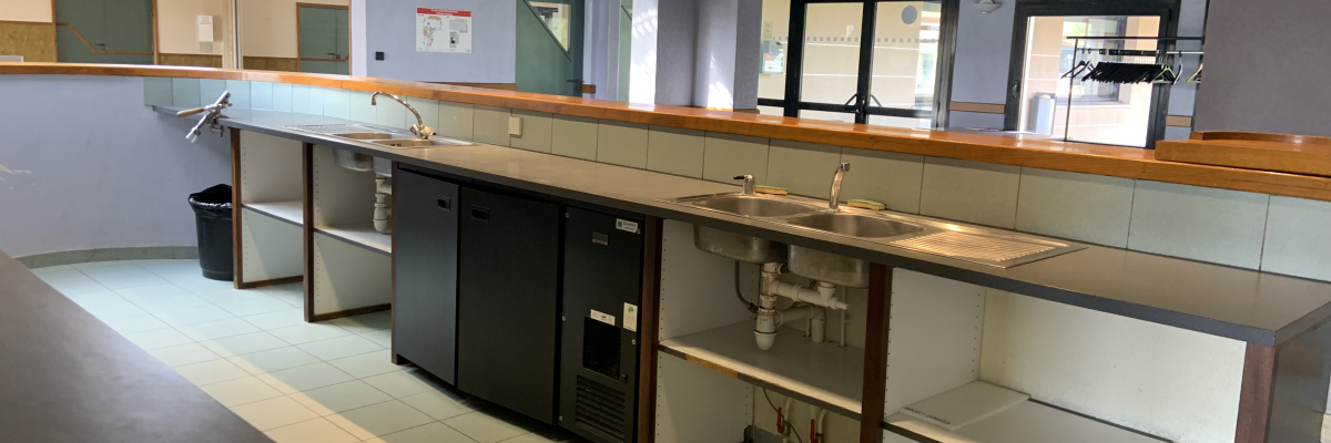 Laboratoire avec paillasse, étagères, évier, frigo, armoires et poubelle.