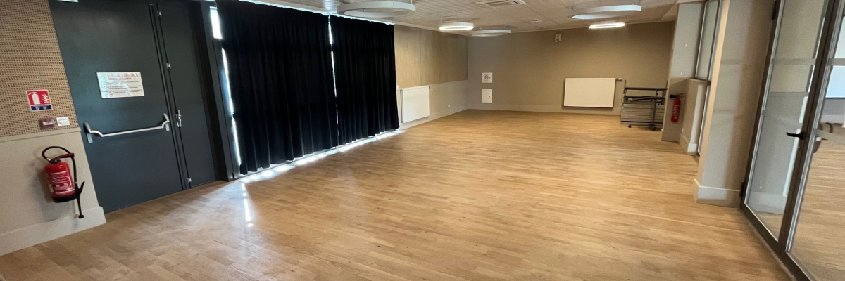 Salle vide avec portes, lumières rondes, sol en bois et extincteur.