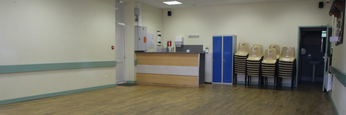 Salle avec comptoir, armoires, chaises empilées, porte et extincteur.