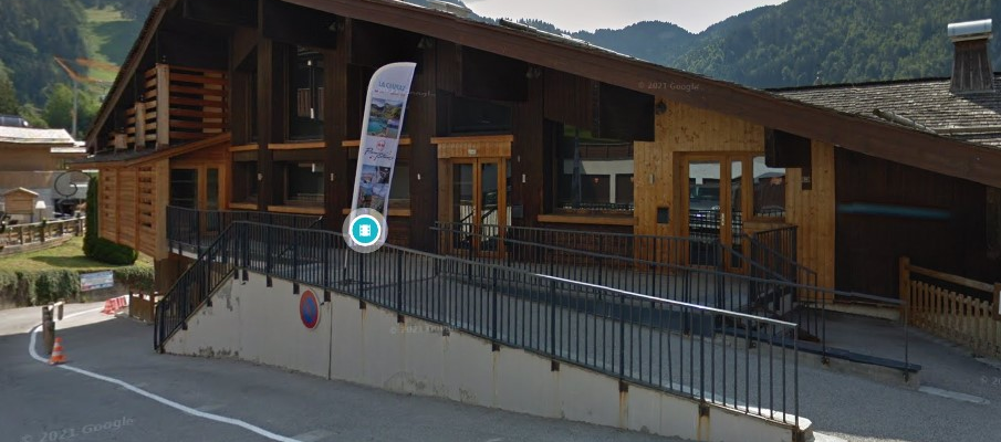 Bâtiment en bois avec terrasse, escalier, rampe, et une affiche indique "Combloux".