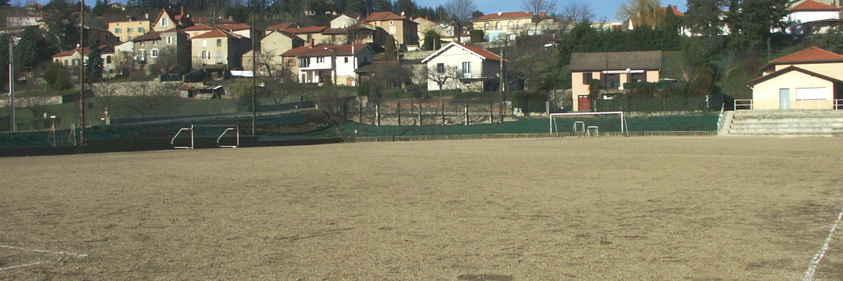 Terrain de football avec buts, clôture, maisons et église en arrière-plan.