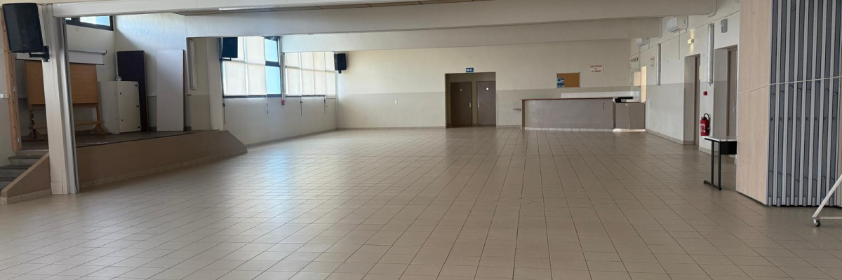 Salle vide avec sol carrelé, portes, fenêtres et distributeur automatique.