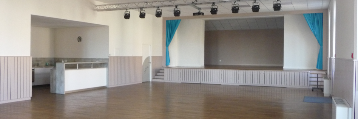 Salle spacieuse avec projecteurs, scène, comptoir et plancher en bois.