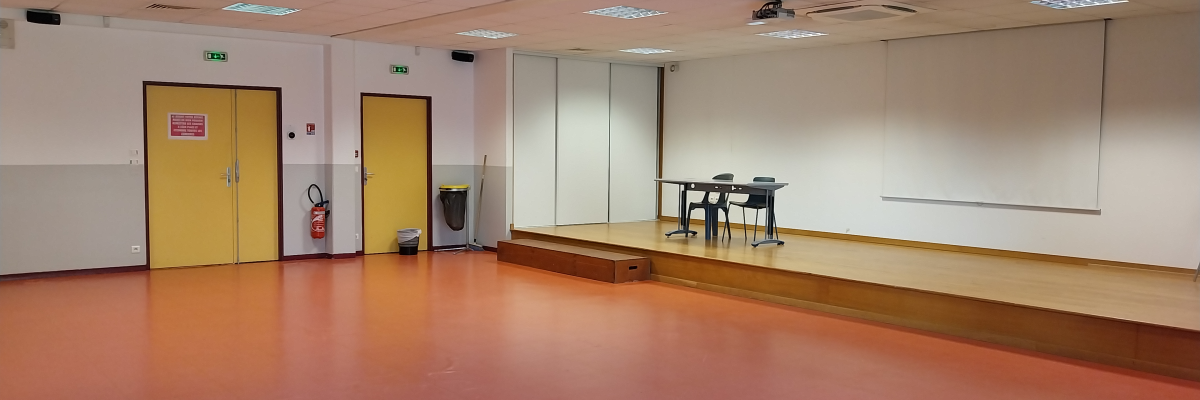Salle avec tables, chaises, tableau, placard, portes et extincteur.