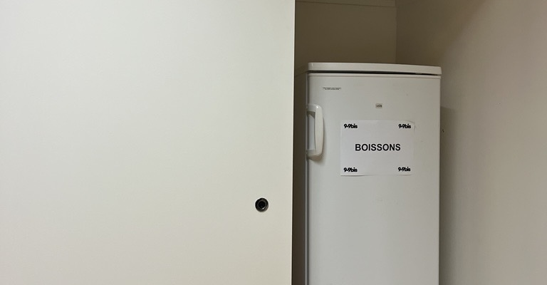 Armoire avec étagères, frigo et produits de nettoyage.