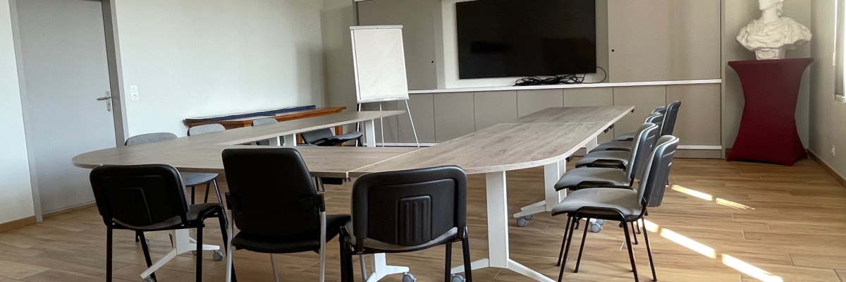 Salle de réunion avec grande table, chaises, télévision, tableau blanc et horloge.