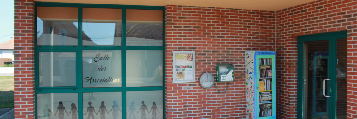 Bâtiment avec porte vitrée, affiches, boîte aux lettres et vitrine.