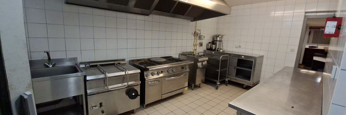 Cuisine professionnelle avec plans de travail, plaques de cuisson, fours, évier, hotte et étagères.