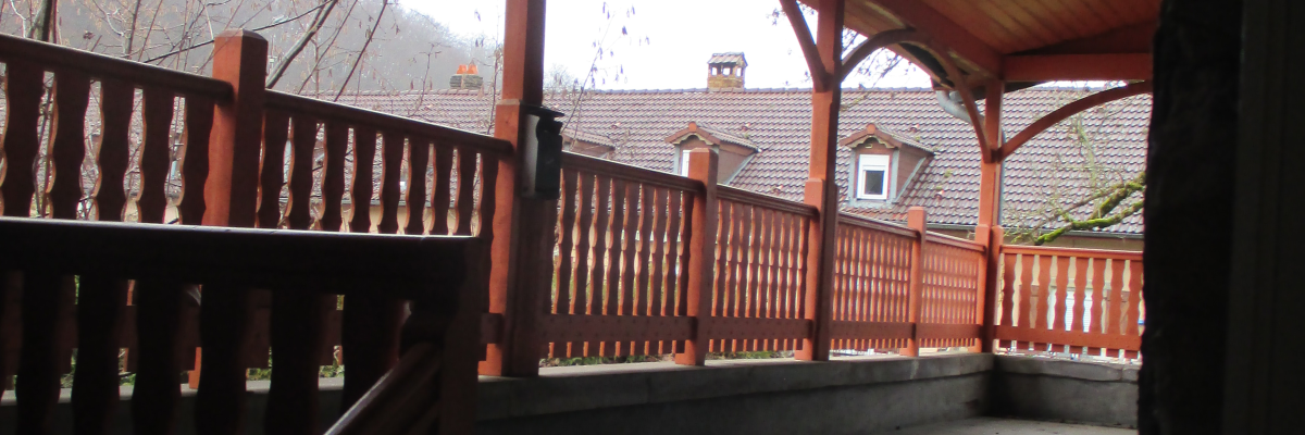 Terrasse en bois avec rambarde, toit et vue sur des bâtiments au loin.