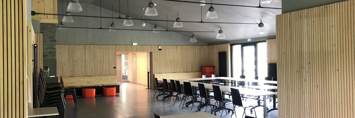 Salle avec tables, chaises, ordinateur, luminaires et poufs.