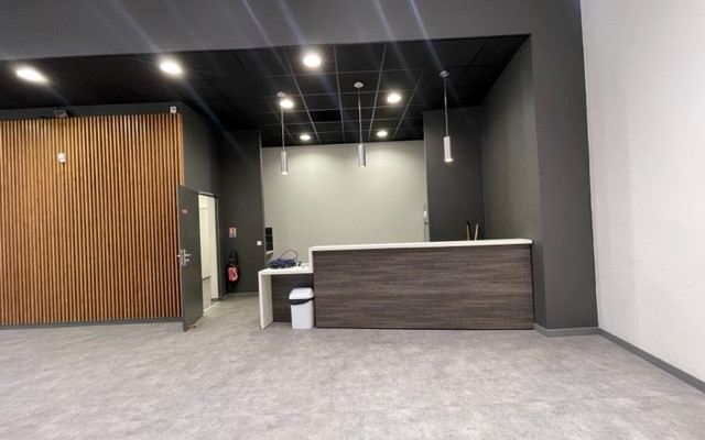 Réception avec comptoir, porte en bois, poubelle, extincteur, unités murales, lumières et porte blanche.