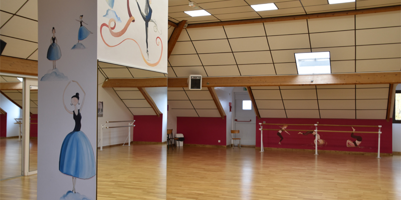 Salle de danse avec barres, miroirs, mur rouge et parquet.