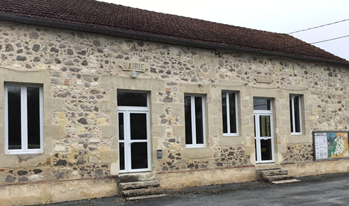 Bâtiment en pierre avec trois fenêtres, une porte centrale et un panneau mural.