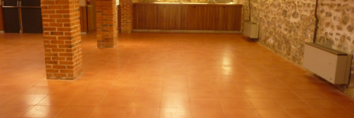 Grande salle avec colonnes en briques, carrelage au sol, éclairage au plafond, murs en pierre et radiateur.