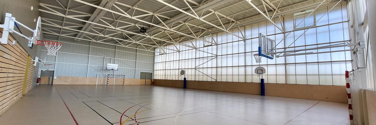 Salle de sport avec paniers de basket, tracés de sol et éclairage suspendu.