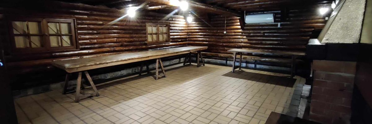 Pièce en rondins, sol carrelé, bancs en bois, table, petite fenêtre.