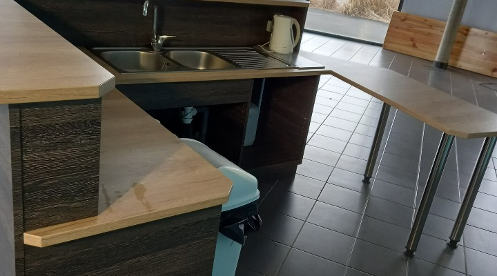 Cuisine avec plan de travail, évier, poubelle, tables et chaises.