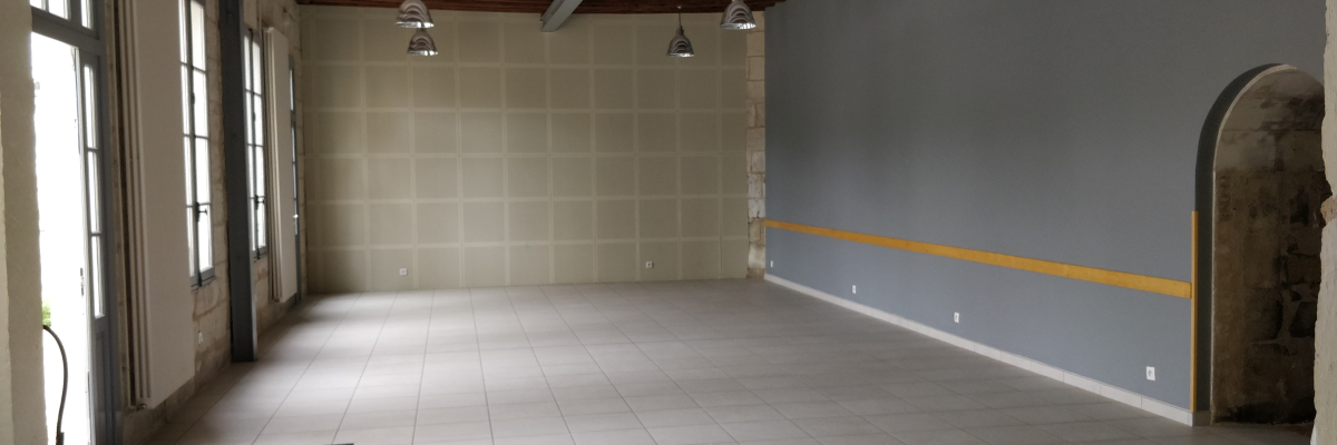 Salle vide avec sol carrelé, murs peints, plafonnier, prises électriques et porte.
