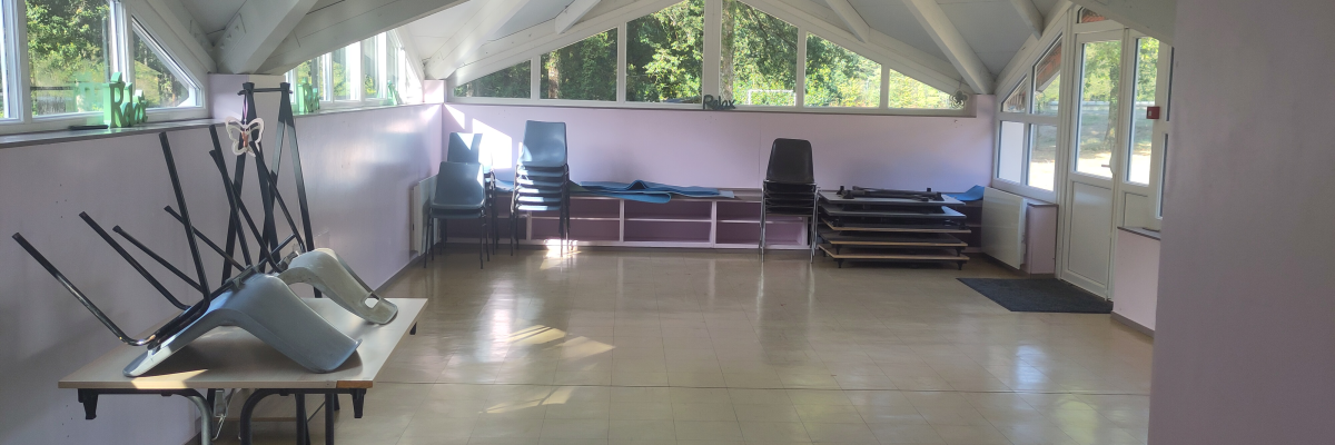Salle avec tables pliantes, chaises, et grandes fenêtres.