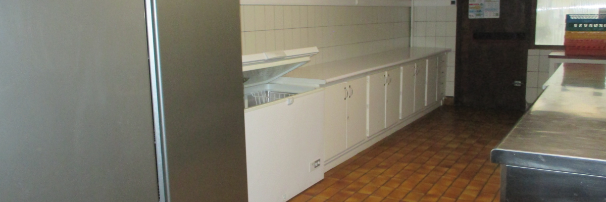 Cuisine avec réfrigérateur, plans de travail, meubles de rangement, évier et sol carrelé.