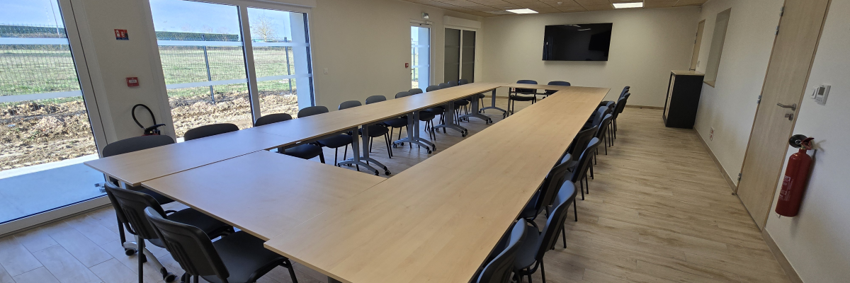 Salle de réunion avec table, chaises, écran et extincteur.