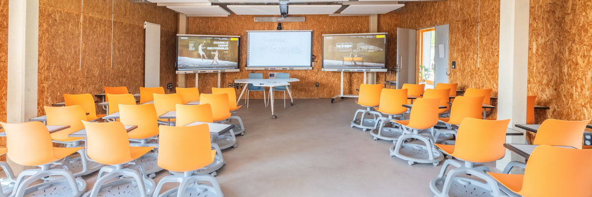 Salle de classe avec tableau blanc, projecteur, tables, chaises, ordinateur et fenêtres.
