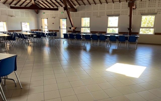 Salle avec tables, chaises, fenêtres et lumière naturelle.