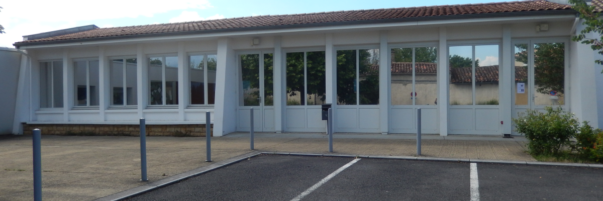 Bâtiment avec grandes fenêtres, toit en tuiles, parking avec places marquées.