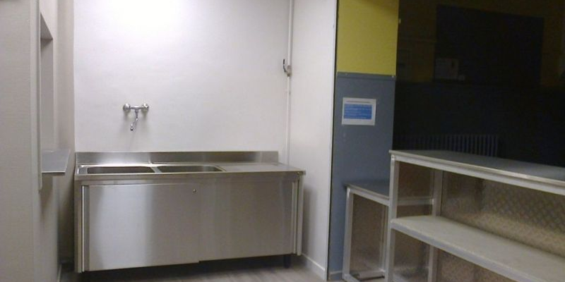 Cuisine avec évier, plans de travail, étagères et réfrigérateur.