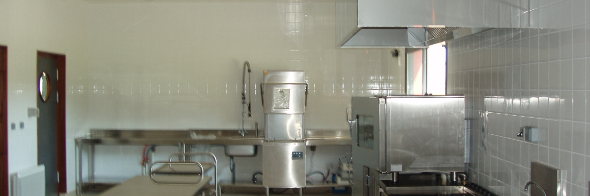 Cuisine professionnelle avec plans de travail, éviers, fours, hotte, et réfrigérateur.