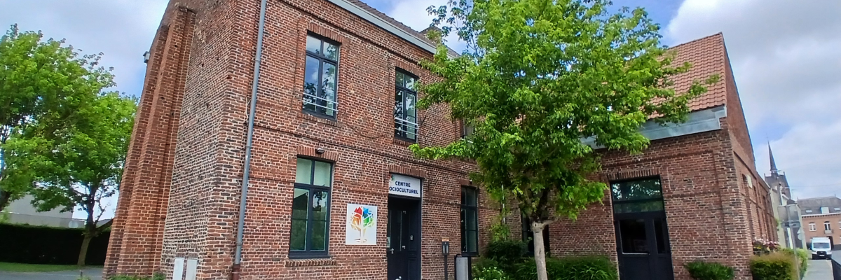 Bâtiment en brique avec entrées, arbres, plantes en pot, parking.