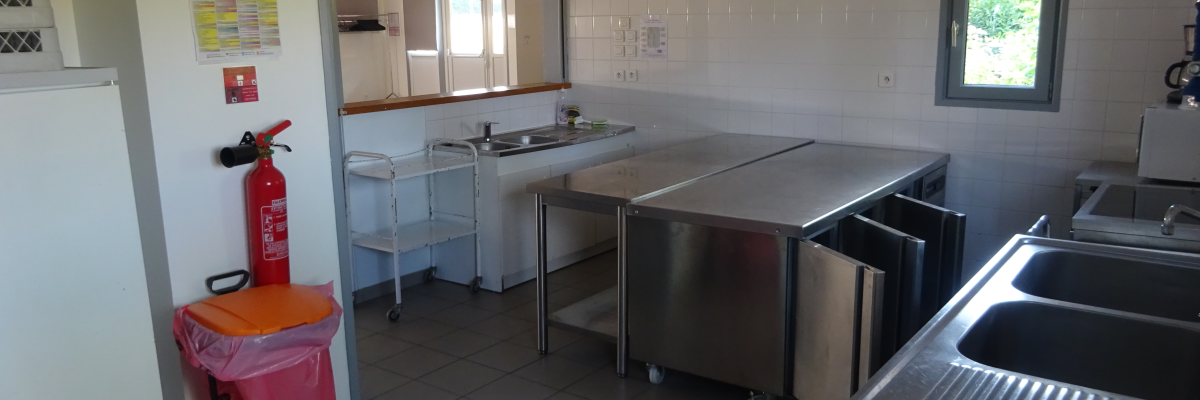 Cuisine avec plans de travail, éviers, chariots de service, extincteur et poubelles.