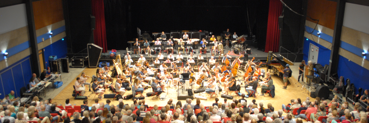Salle de concert avec public, orchestre, instruments et projecteurs.