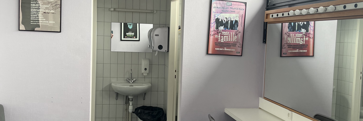 Salle avec lavabo, miroir, poubelle, chaise, et affiches murales.