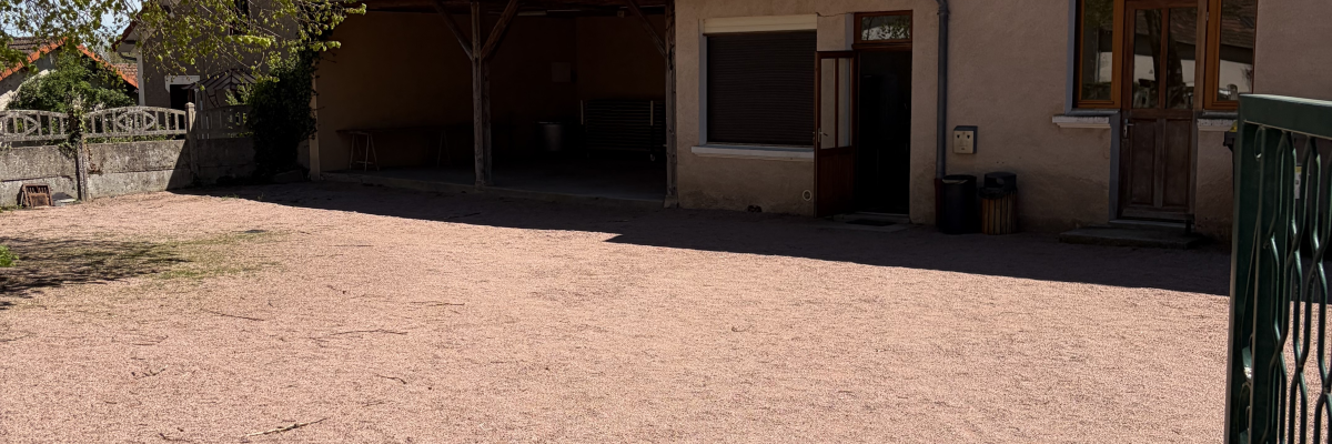 Maison avec cour en gravier, arbre, portail et barbecue.