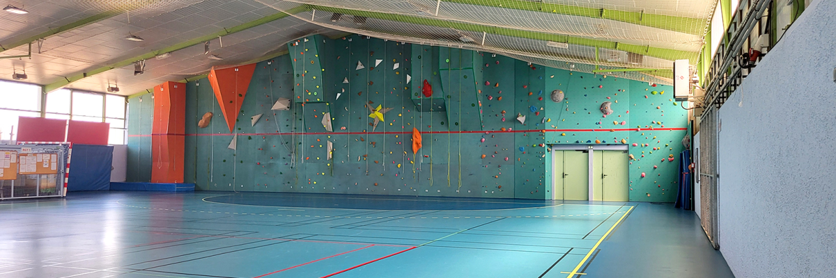 Salle de sport avec mur d'escalade, sol de jeu, et matériel d'escalade.