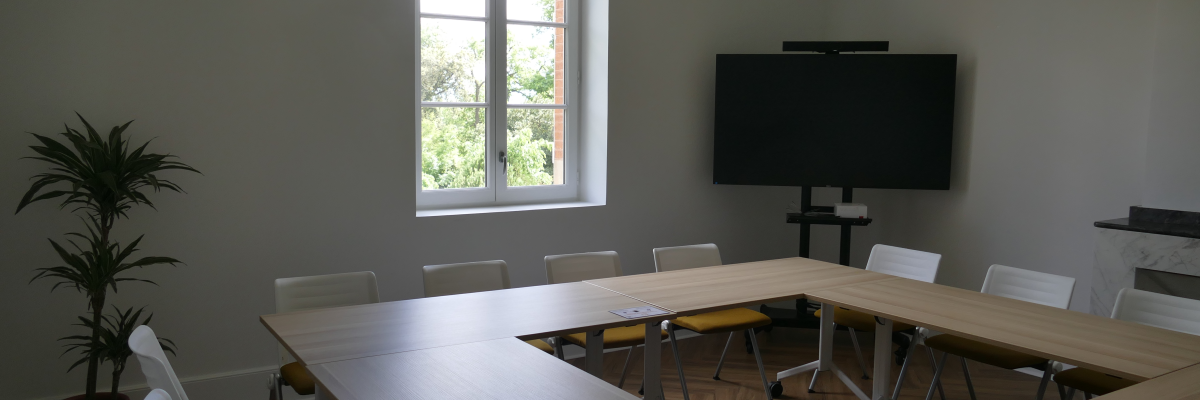 Salle de réunion avec table, chaises, écran et fenêtre.
